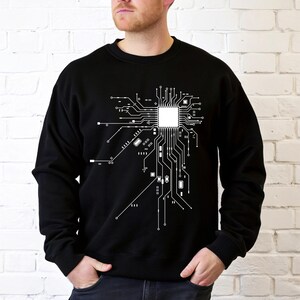 May include: Black sweatshirt featuring a white circuit board design. The graphic depicts a detailed representation of a computer processor and its interconnected components, ideal for tech enthusiasts.