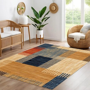 May include: A rectangular area rug with a geometric pattern. The rug features squares and rectangles in shades of gold, navy blue, red, and light blue. The design incorporates both solid colors and striped sections, creating a modern aesthetic.
