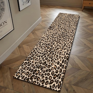 Puede incluir: Una alfombra rectangular con estampado de leopardo. La alfombra presenta un fondo beige con manchas marrones y negras. La alfombra está colocada sobre un suelo de madera.