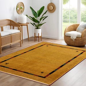 May include: A rectangular mustard-yellow area rug with a dark border and corner accents. The rug features a red border and black and green stripes. The rug is placed on a hardwood floor in a living room setting.