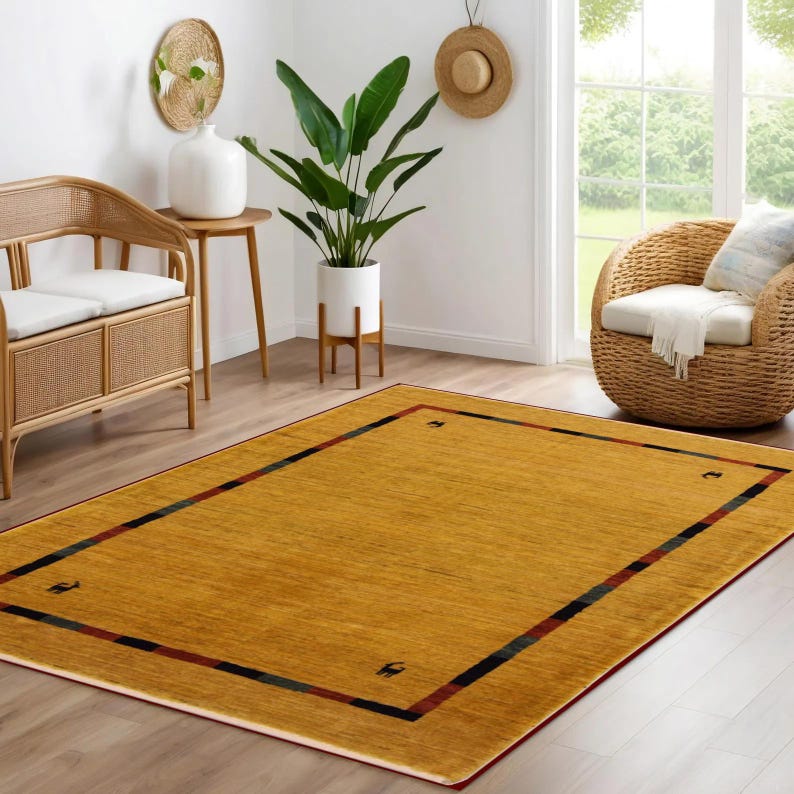 May include: A rectangular mustard-yellow area rug with a dark border and corner accents. The rug features a red border and black and green stripes. The rug is placed on a hardwood floor in a living room setting.