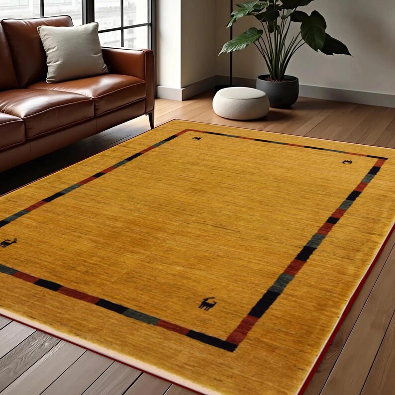 May include: A rectangular, mustard-yellow area rug with a patterned border. The border features a thin red line, followed by a black, green, and blue stripe. Small, dark animal silhouettes are placed around the border. The rug is placed on a hardwood floor.