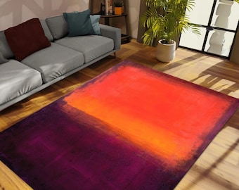 May include: A rectangular area rug with an abstract design. The rug features a gradient of colors, transitioning from deep purple at the bottom to vibrant orange at the top. The rug is placed on a hardwood floor.