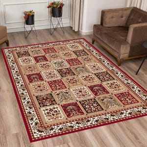 Può includere: Un tappeto rettangolare con un bordo rosso e un motivo ripetuto di quadrati. I quadrati presentano disegni floreali nei toni del rosso, beige e nero. Il tappeto è posato su un pavimento in legno e lo stile generale è tradizionale.