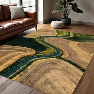May include: Area rug with a landscape design featuring a winding road through fields of brown and green. The rug has a rectangular shape and is placed on a wooden floor. The design evokes a sense of nature and tranquility.