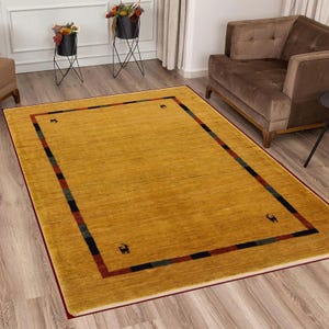 May include: Mustard yellow rectangular area rug with a border of red, black, and green stripes. The rug has a simple design with small animal silhouettes in each corner. The rug is placed on a hardwood floor.
