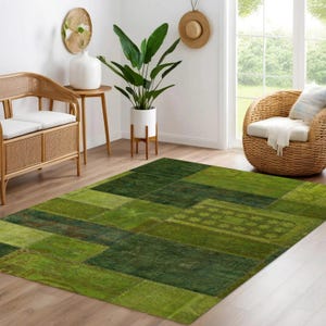 May include: A green patchwork rug with various shades of green squares and rectangles. The rug is placed on a light-colored wooden floor in a room with natural light and wicker furniture.