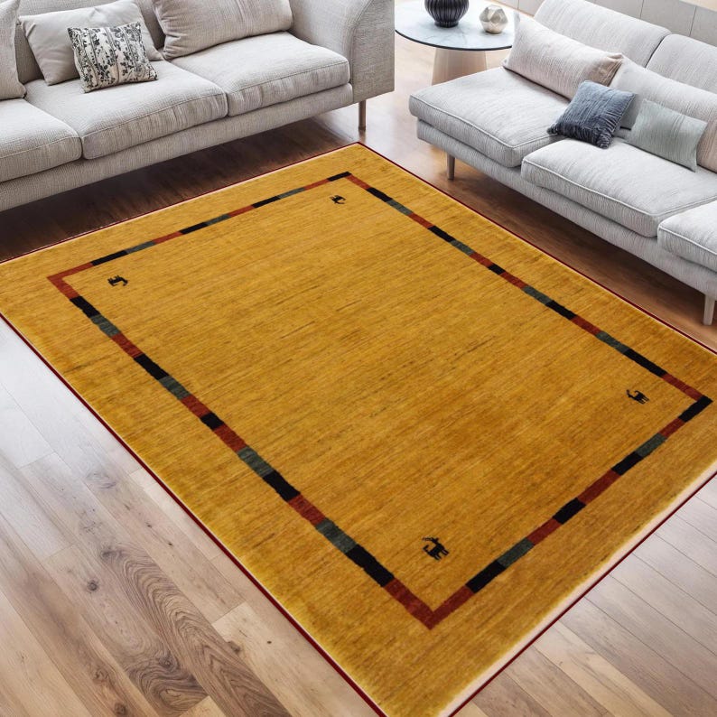 May include: Mustard yellow rectangular area rug with a border of black, green, and red stripes. The rug has a simple design with small black symbols in each corner. The rug is placed on a hardwood floor.