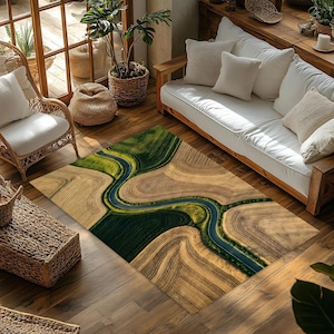 May include: Rectangular area rug with an aerial view design of a river winding through fields. The rug features shades of green, brown, and blue, creating a natural landscape pattern. The rug is placed on a wooden floor.