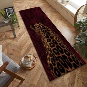 Puede incluir: Una alfombra rectangular tipo pasillero con un fondo color burdeos intenso y un sutil patrón de rosas tonales. El diseño central muestra un estampado de leopardo grande y detallado en tonos dorados, marrones y negros a lo largo.