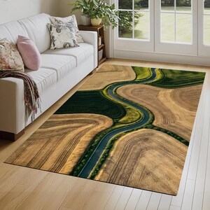 May include: Area rug featuring an aerial view of a winding road through a landscape of fields. The rug's design includes shades of brown, green, and blue, creating a naturalistic and scenic pattern. The rug is rectangular and placed on a hardwood floor.