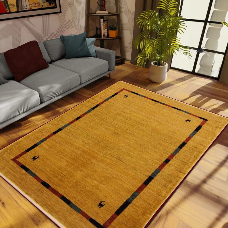 May include: A rectangular, golden-yellow area rug with a patterned border. The border features a red, blue, and black stripe design, with small black animal silhouettes in each corner. The rug is placed on a hardwood floor.