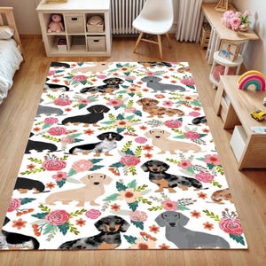 May include: A rectangular area rug featuring a repeating pattern of dachshund dogs in various colors, interspersed with floral arrangements of pink and orange flowers on a white background. The rug is designed for indoor use.