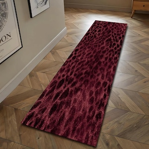 May include: A rectangular burgundy rug with a dark, textured pattern resembling animal hide. The rug is placed on a wooden floor, adding a touch of warmth and style to the space. This decorative rug is suitable for hallways and entryways.