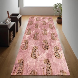Op de afbeelding: Een rechthoekig roze tapijt met een marmerachtige textuur en een herhalend patroon van cheeta's. De cheeta's worden afgebeeld in een zittende positie met gebogen ruggen en gekrulde staarten. Het tapijt ligt op een houten vloer.