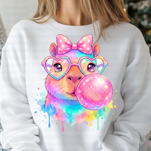Puede incluir: Sudadera blanca con una ilustración colorida de una llama con gafas en forma de corazón y un lazo de lunares. La llama está soplando una burbuja rosa, con salpicaduras de pintura de acuarela.