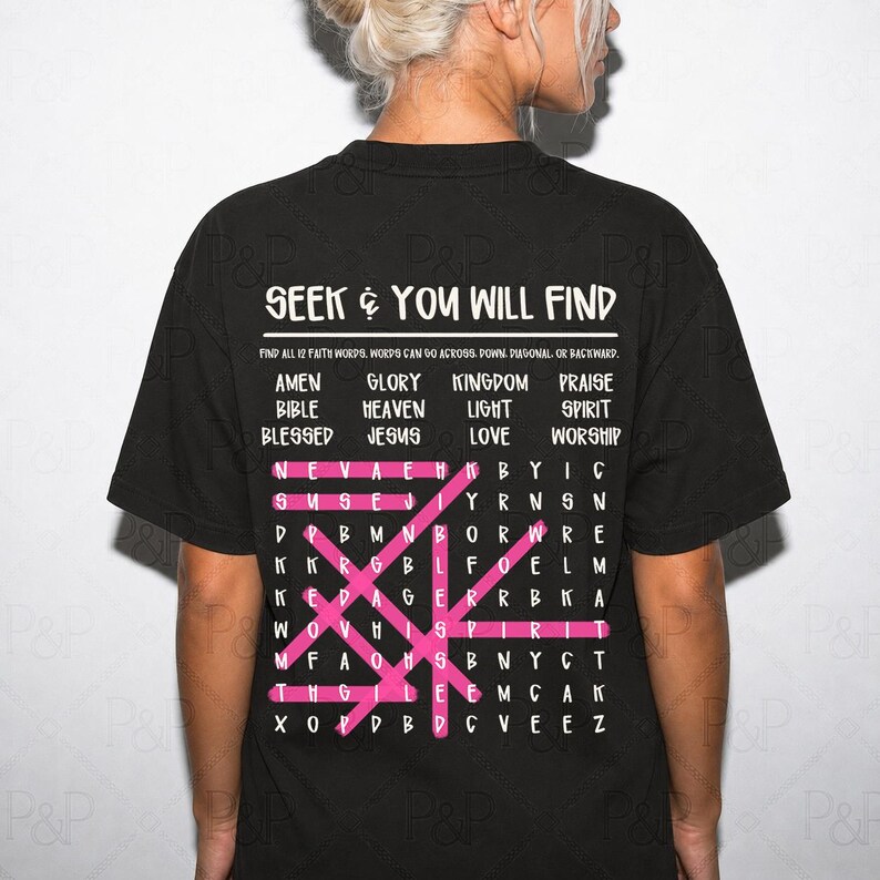 May include: A black t-shirt featuring a white word search puzzle graphic on the back. The text reads SEEK & YOU WILL FIND, followed by a list of 12 faith words and a grid of letters with several words highlighted by pink horizontal and diagonal lines.