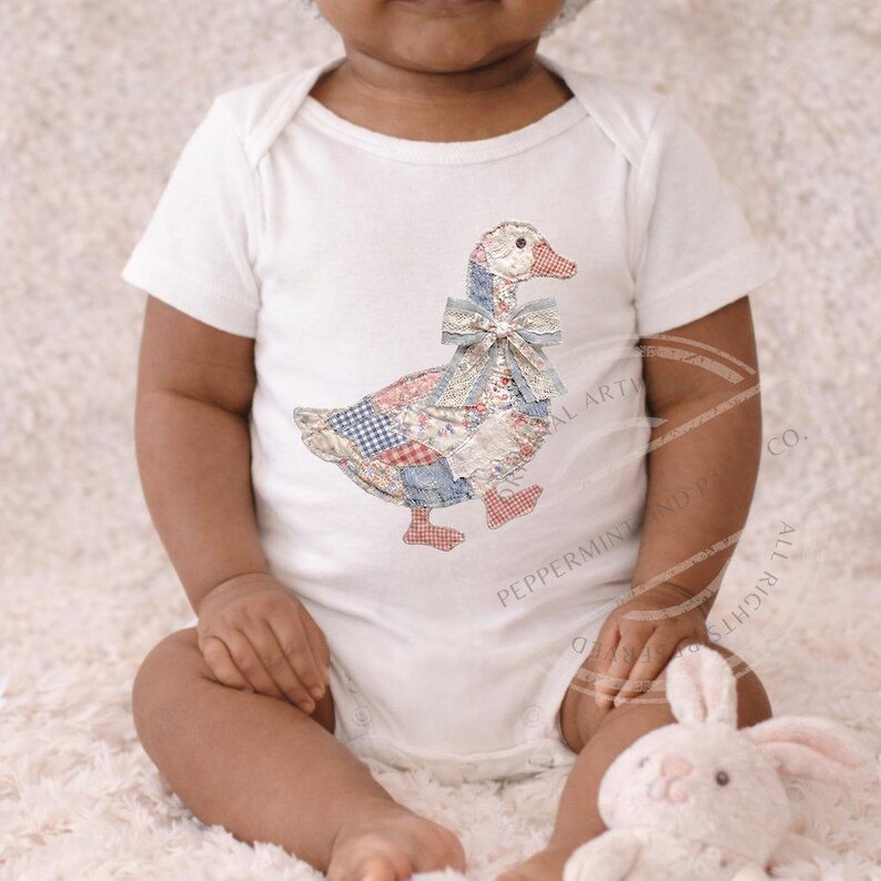 May include: White baby onesie featuring a patchwork goose design with a blue bow. The goose has a red, white, and blue patchwork pattern. The onesie is short-sleeved and has a simple, classic design.