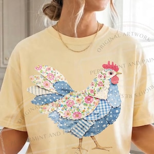 May include: A light yellow t-shirt featuring a patchwork rooster design. The rooster has a red comb, blue and white patterned feathers, and a floral patterned body. The shirt has a relaxed fit.