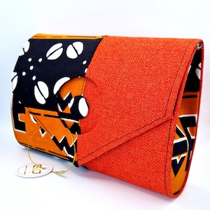 Op de afbeelding: Een rechthoekige clutch met een klepsluiting. De clutch heeft een levendige oranje textuurstof aan de voorkant en een patroonstof met zwarte, witte en oranje ontwerpen aan de zijkant. Een ronde knoop zet de flap vast.