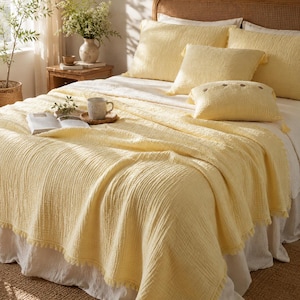 May include: A light yellow bedding set featuring a textured, crinkled fabric finish. The set includes a large throw blanket with fringed edges, two square pillow shams, and a rectangular accent pillow adorned with three small, dark brown buttons.