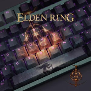 Puede incluir: Un teclado mecánico con teclas de color gris oscuro y un marco verde. El teclado presenta el texto "ELDEN RING" en dorado, con teclas iluminadas en naranja y morado. Una barra espaciadora personalizada muestra una figura de guerrero.