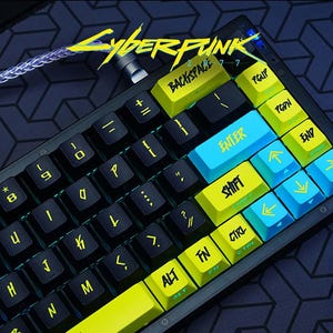 Può includere: Una tastiera meccanica con tasti neri e accenti giallo neon e blu. La parola "Cyberpunk" è in giallo in alto a sinistra. I tasti includono "Enter", "Shift" e "Backspace".