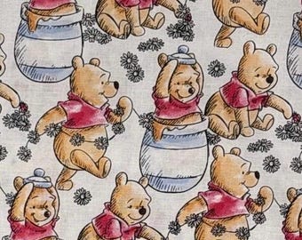 Puede incluir: Una tela de color claro con un patrón repetitivo de personajes de Winnie the Pooh con camisetas rojas. Los osos aparecen en varias posturas, incluyendo sentados dentro de tarros de miel con rayas azules y sosteniendo guirnaldas de pequeñas margaritas blancas.