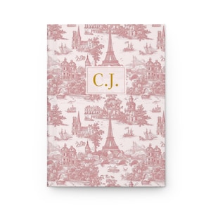 May include: A hardcover journal with a pink and white toile pattern featuring Parisian landmarks. The journal cover has a gold-colored rectangle with the initials "C.J." printed in gold.