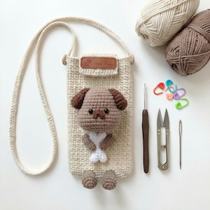以下が含まれることがあります： 茶色の犬のデザイン、クリーム色のストラップ、革製のタグに「Hand Made」の文字が入った、クリーム色のかぎ針編みの携帯電話ケース。糸、かぎ針編みフック、はさみ、ステッチマーカーが含まれています。