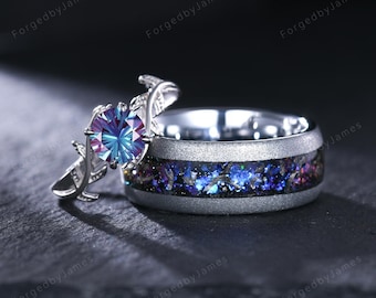May include: A silver engagement ring and wedding band set. The engagement ring features a large, multi-colored gemstone and a floral design. The wedding band has a dark blue and purple inlay with a silver band.