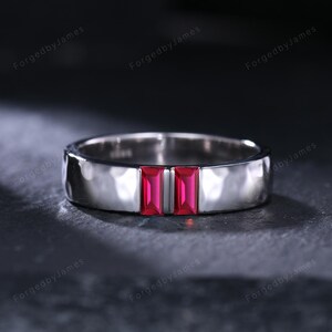 Könnte beinhalten: Ein silberner Ring mit gehämmertem Muster und zwei rechteckigen, leuchtend roten Edelsteinen. Der Ring hat eine polierte Oberfläche und ein modernes Design, geeignet für den Alltag oder besondere Anlässe.