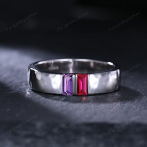 May include: A silver ring with a hammered texture, featuring two rectangular gemstones: a purple amethyst and a red ruby. The ring is set against a dark background.