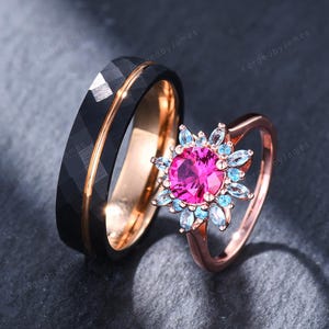 May include: A black faceted band with a rose gold interior and a rose gold ring featuring a central round pink stone surrounded by a halo of small light blue marquise-cut stones. The text ForgedbyJames is visible in the background.