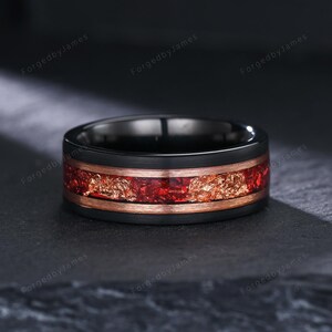 Puede incluir: Anillo negro con una banda color cobre y una incrustación central de materiales rojos y dorados. El anillo tiene un diseño moderno y elegante, adecuado para diversas ocasiones. El ancho del anillo es de aproximadamente 0,8 cm.