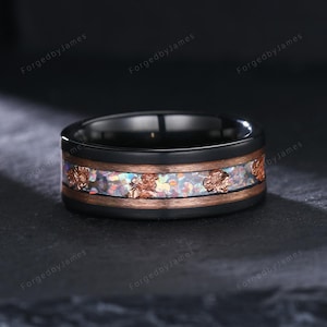 May include: Black ring with a copper and opal inlay. The ring has a black band with a copper-colored band in the middle. The inlay features iridescent opal and copper-colored accents. The ring is a piece of jewelry.