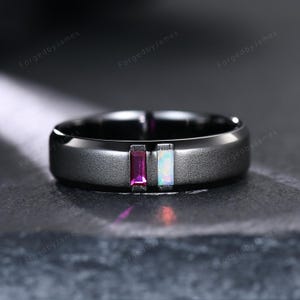 May include: A black ring with a matte finish, featuring two rectangular gemstones: a deep magenta and an iridescent opal. The ring has a smooth, rounded band and is set against a dark background. The text "ForgedbyJames" is repeated around the ring.