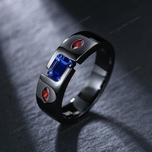 Könnte beinhalten: Ein schwarzer Ring mit einem rechteckigen blauen Edelstein und zwei ovalen roten Edelsteinen. Der Ring hat ein modernes Design mit geteiltem Band. Der Text "ForgedbyJames" ist sichtbar.