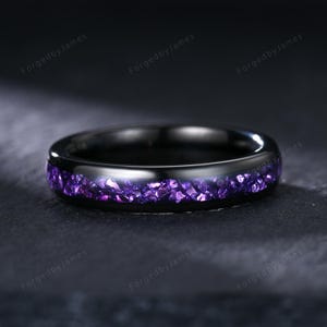May include: A black ring with a band of crushed purple gemstones. The ring has a polished, reflective surface. The text "ForgedbyJames" is repeated around the ring.
