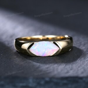 Puede incluir: Un anillo de oro con un ópalo de talla marquesa engastado horizontalmente en el centro. El ópalo muestra destellos iridiscentes de luz rosa, azul y verde. La banda es de oro liso y pulido con un diseño cónico que rodea la piedra.