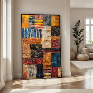 May include: Large framed artwork featuring a patchwork design with a variety of textures and colors. The artwork includes rectangular blocks in shades of blue, yellow, orange, red, and black. The frame is black, and the artwork is leaning against a white wall.
