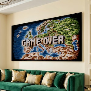 Op de afbeelding: Een ingelijst kunstwerk met een gepixeld kaart van Europa met de tekst "GAME OVER" in een retro videogame-stijl. Het kunstwerk gebruikt blauwe, groene en bruine tinten, geplaatst in een zwart frame. Het hangt boven een groene fluwelen bank.