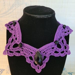 May include: Purple crocheted necklace with black beads and a large black teardrop-shaped pendant.