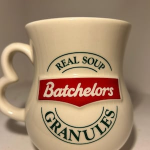May include: Cream ceramic mug with a heart-shaped handle. The mug has the text "REAL SOUP" above a red banner with "Batchlors" in white, and "GRANULES" below in green. A vintage-style kitchenware item.
