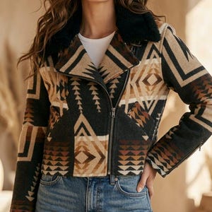 May include: A cropped jacket featuring a geometric pattern in shades of black, tan, and brown. The jacket has a black faux fur collar, a silver-toned metal zipper closure, long sleeves, and is worn over a white shirt and blue denim jeans.