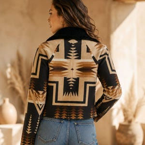 May include: A long-sleeve jacket featuring a black, tan, and brown geometric pattern with a black faux-shearling collar. The jacket is worn with blue denim jeans. The back view shows the intricate angular design across the shoulders and sleeves.
