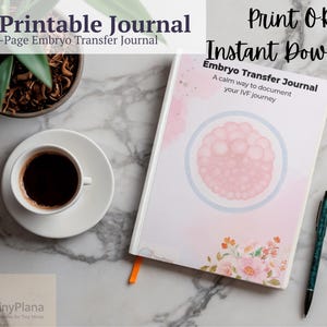 Könnte beinhalten: Ein IVF-Druckjournal mit dem Text "Embryo Transfer Journal" und "A calm way to document your IVF journey". Das Journal ist geöffnet, neben einem Stift, einer Tasse Kaffee und einer kleinen Pflanze in einem Topf. Das Journal hat ein rosa und florales Design.