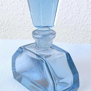 Può includere: Un decanter in vetro azzurro con base rettangolare dai bordi smussati e un tappo sfaccettato abbinato. Il contenitore ha un aspetto chiaro e traslucido con una finitura liscia e una forma geometrica distinta dal colore uniforme.