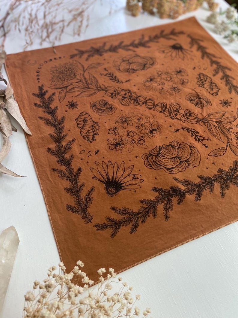 May include: A brown bandana with a black floral design. The design includes flowers, leaves, and other botanical elements. The bandana has a fringed edge.