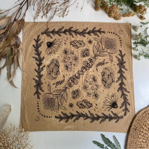 May include: A tan bandana with a black and white floral design. The design features flowers, leaves, and stars. The bandana is made of a soft, cotton fabric.